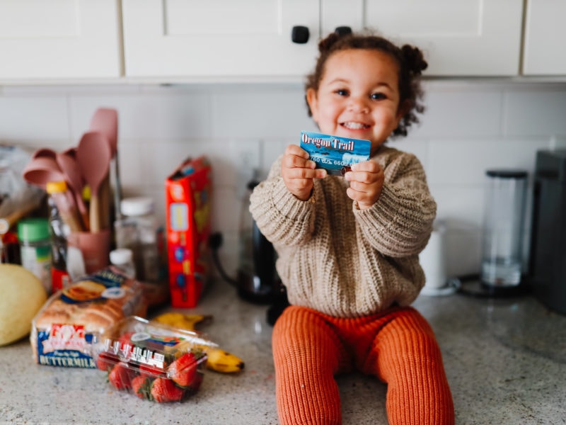 Smiling child holding an Oregon EBT card, symbolizing restored SNAP benefits and food access